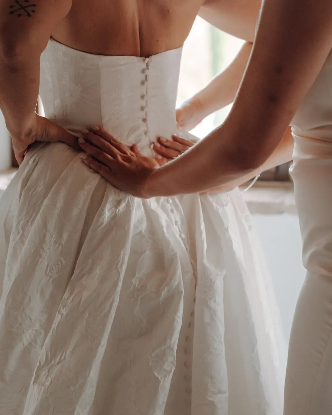 Bride getting ready, the back of her wedding dress being fastened